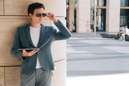 Stylish young man in sunglasses holds a digital tablet against the backdrop of the city background. Theの写真素材