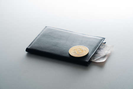 A man's black purse on a white insulated background. Bitcoin coin on top on a dark purseの写真素材