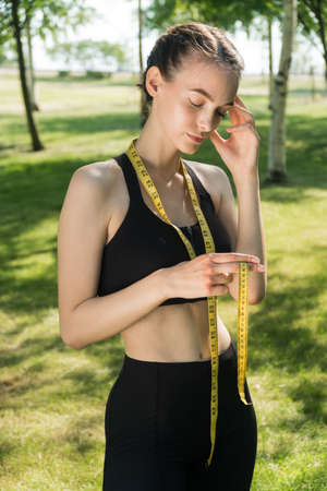 Sad slender girl holds a centimeter tape in her hands. The concept of improper weight loss woman fitness trainerの写真素材