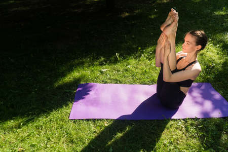 A girl in outdoor sportswear does an exercise for weight loss. Yoga, concept functional training using a rug at sunsetの写真素材