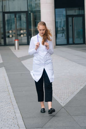 A young girl doctor in a white robe goes against the background of the medical clinicの写真素材