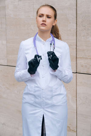 Portrait of a doctor of a woman in a medical gown and protective gloves, which holds a stethoscopeの写真素材