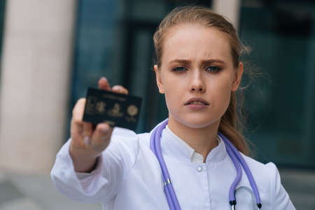 Portrait of a sad tired girl doctor holding a plastic card in front of the cameraの写真素材