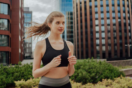 A young blonde sports girl in a black suit runs along modern housesの写真素材