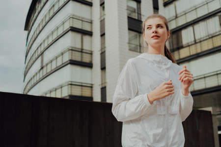 A young blonde sports girl in a black suit runs along modern housesの写真素材