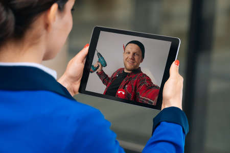 View from the back of girl talking by video link with a builder during the renovationの写真素材