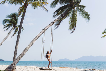 Beautiful thin woman swinging on a swing on paradise beach with nobodyの写真素材
