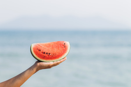 Girl holding a piece of watermelon in hand by the seaの写真素材