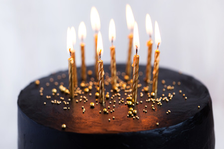 Black round birthday cake with burning golden candles on white backgroundの写真素材