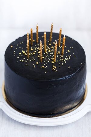 Black birthday cake with golden candles on white backgroundの写真素材