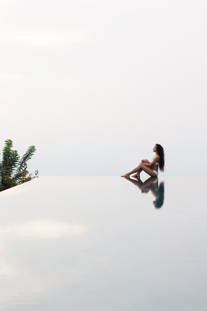 Young slim woman posing on the edge of luxury infinity poolの写真素材
