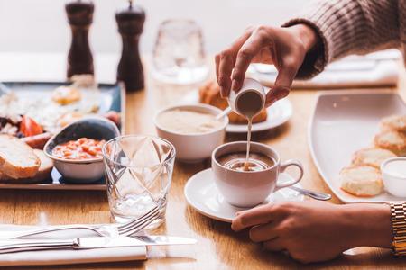 Girl pouring milk in coffee at breakfastの写真素材