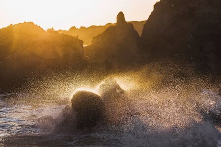 Waves crashing on rocks in sunlight