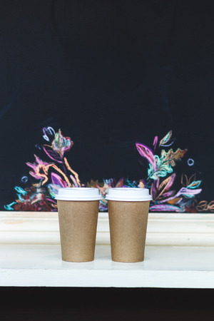 Two carton paper cups with cap at the bar with autumn patternの写真素材
