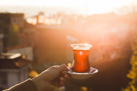 Hand holding a cup of traditional Turkish tea illuminated and transparent by the warm evening sunlight.の写真素材