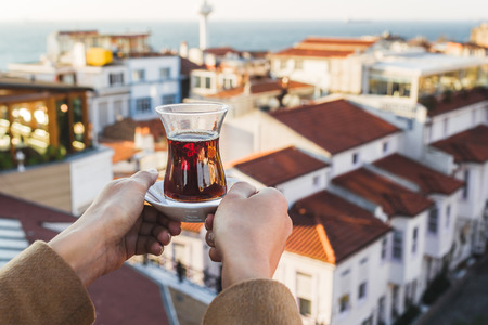 Hand holding a cup of traditional Turkish tea illuminated and transparent by the warm evening sunlight.の写真素材