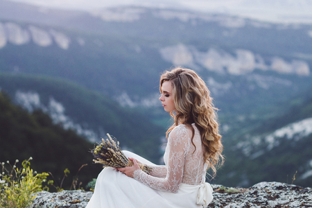 Portrait of young curly woman on a background of mountains at sunset. Wedding bouquet in handsの写真素材