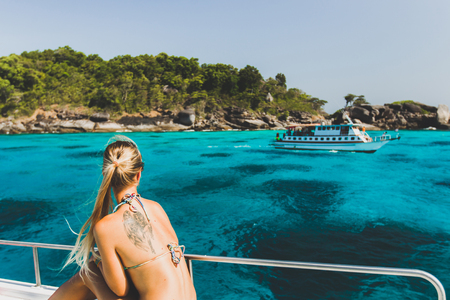 Blonde woman with tattoo on back relaxing on luxury yacht with view of paradise tropical island with turquoise waterの写真素材