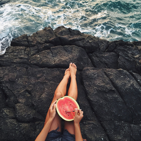 Woman eat watermelon on beach. Stone edge of cliffの写真素材