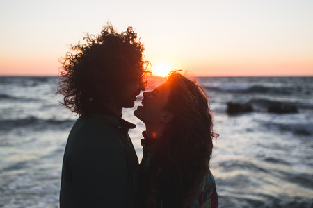 Young hipster couple with long curly hair kissing at sunset. Sensual close-up portraitの写真素材