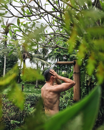 Handsome tanned muscular man taking shower outdoor in tropical garden in Bali, organic skin care, luxury spa hotel, lifestyle photoの写真素材
