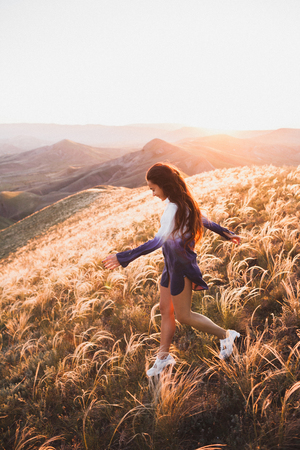 Happy young woman running on feather grass field in sunset light. Nature lifestyle and amazing view around. Long black hair with colored locksの写真素材