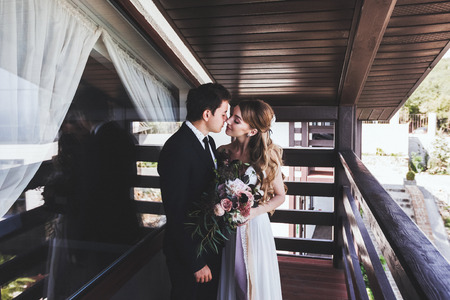 Groom kisses bride on the balcony of villa. Young stylish coupleの写真素材