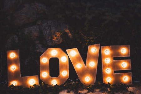 Word love consisting of the letters highlighted with bulbs standing on lawn at nightの写真素材