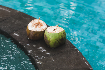 Two young fresh coconuts on edge of swimming pool with crystal clean emerald water. Tropical and summer moodの写真素材