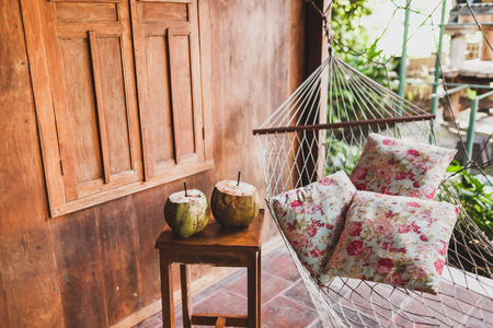 Hammock with colorful pillows and wooden table with two fresh coconuts. Wooden houseの写真素材