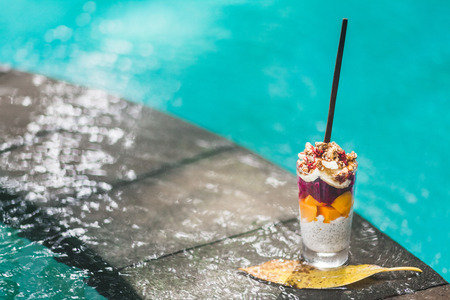 Coconut chia pudding coctail with fresh mango, banana and dragonfruit on edge of pool with clean turquoise water. Tropical styleの写真素材