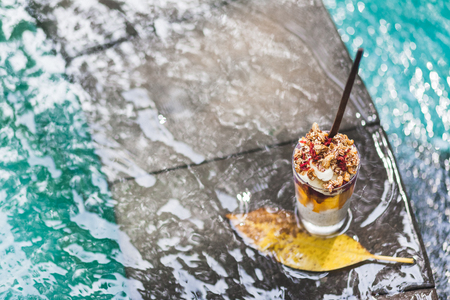 Coconut chia pudding coctail with fresh mango, banana and dragonfruit on edge of pool with clean turquoise water. Tropical styleの写真素材