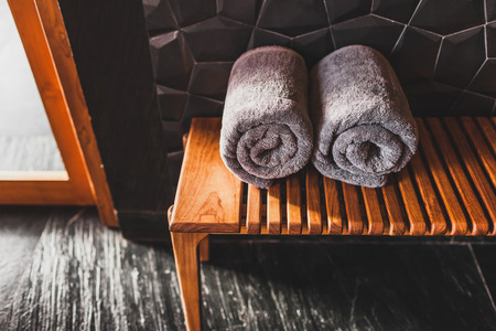 Two rolled grey towels on wooden bench in sauna. Spa in hotel