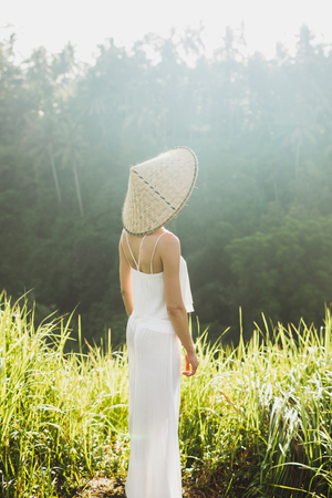 Portrait of young asian woman in traditional balinese straw hat. Morning sun in Ubud rice fields.の写真素材