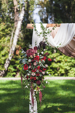 Wedding ceremony in rustic style decorated with different red flowers, white textile and chairs in forestの写真素材