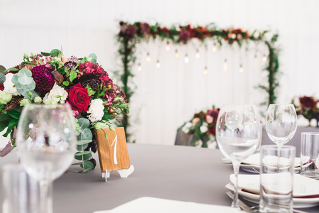 Wedding table, decorated with red flowers bouquets, candles, grey tablecloth, and white platesの写真素材