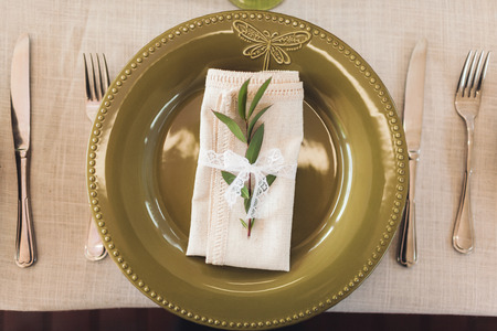 Green decorated cutlery with plant leaves and white napkins on wedding table. Rustic style