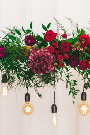 Wedding reception decoration with different electric edison lamps and fresh red and bordo flowers, rustic styleの写真素材