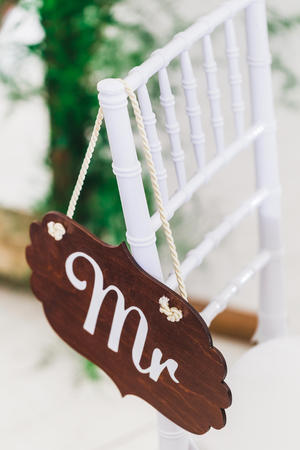 Wooden vintage plate with Mr sign, hanging on rope on white chair on weddingの写真素材