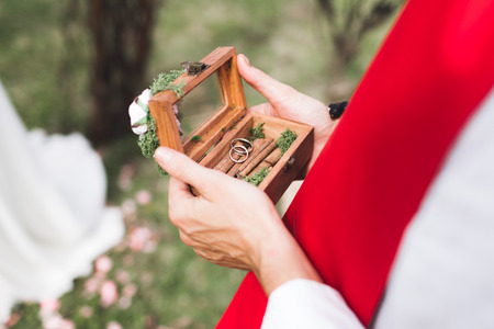 Priest holding wooden vintage box with two rings on cinnamon texture on wedding ceremony