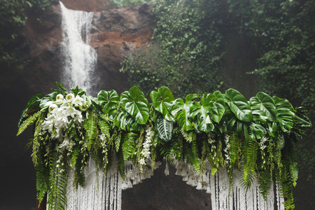 Tropical wedding ceremony with waterfall view. White arch decorated with green jungle leaves monstera and fernの写真素材