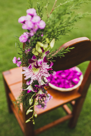 Brown wooden chairs standing on grass on wedding ceremony decorated with pink and purple flowers. Plate with flower petalsの写真素材