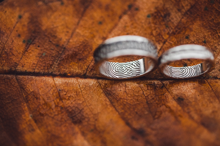Wedding rings with fingerprints close-up on wet brown autumn leaf skeleton textureの写真素材