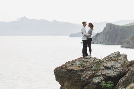 Young couple walking on nordic sea coast with mountain view in spring, casual style clothing sweaters and jeansの写真素材