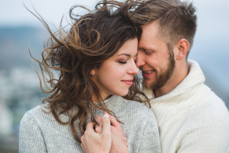 Close-up portrait of couple with wind in hair, hugging and happy together. Both in sweatersの写真素材