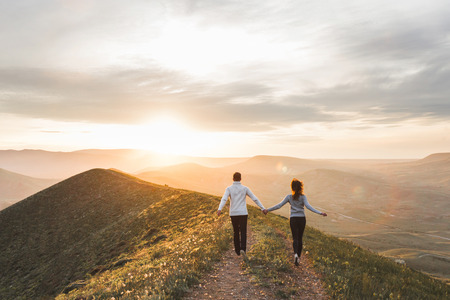 Young couple running together by sunset hill with amazing mountain viewの写真素材