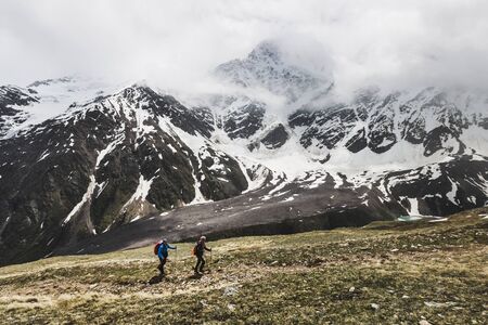 ELBRUS REGION, RUSSIA - JUNE 23, 2017: Two tourists hiking to the top of mount Cheget in Russia. Snowy and foggy landscape around, view of glacier Semerkaのeditorial素材