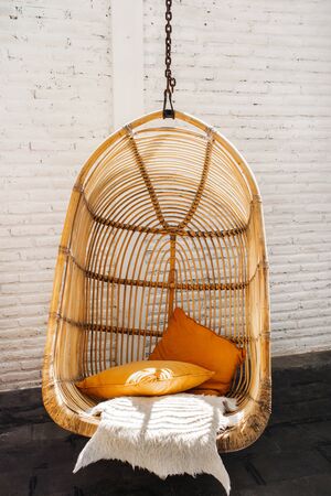 Wicker rattan hanging chair in loft cafe. Eco friendly furniture style and concept. Orange pillows...