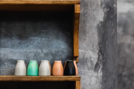 Different colorful coffee cups on wooden shelf in cafe. Background of gray concrete cement wall....