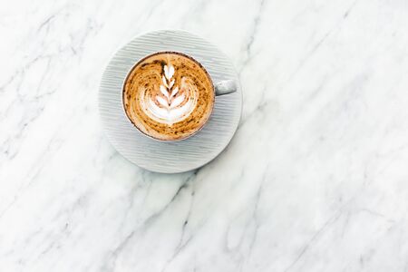 Cup of fresh coffee cappuccino with classic latte art and chocolate on white marble table trendy...